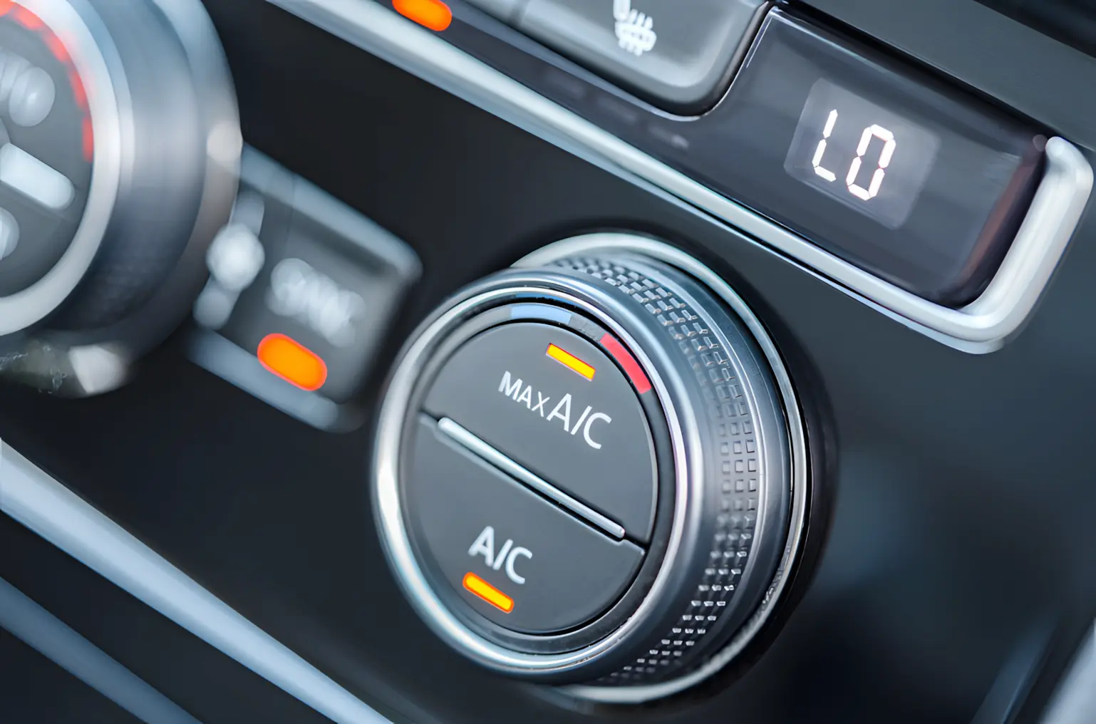 Close-up of a car’s air conditioning control panel, showing a dial with MAX A/C and A/C options, illuminated with orange indicator lights, and a digital display reading LO above the controls.