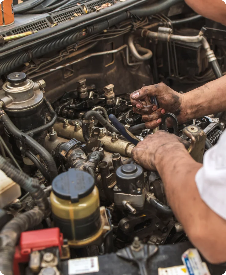 A mechanic with dirty hands works on a car engine, using tools to repair or adjust engine components inside the vehicle’s open hood.
