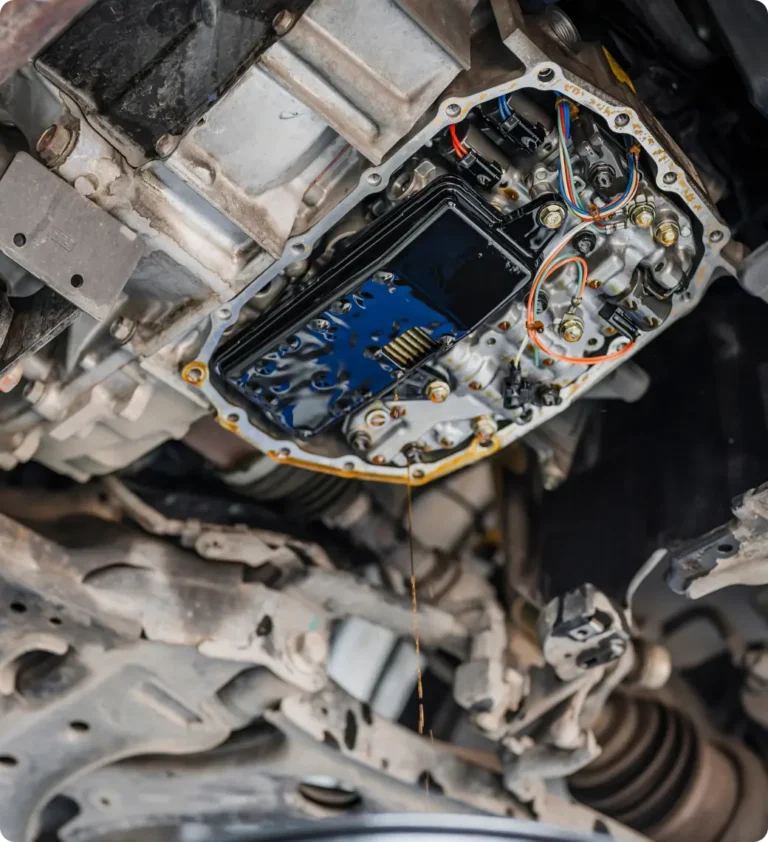 Close-up view of a cars automatic transmission system with the oil pan removed, exposing internal components and wiring, and fluid visibly draining out.