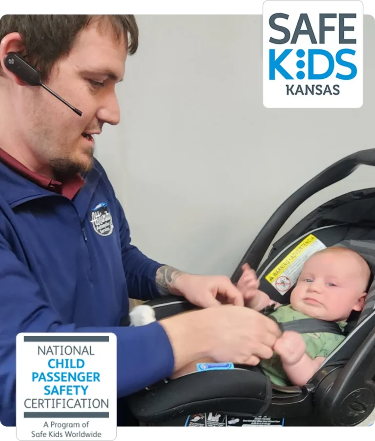 A man with a headset secures a baby in a car seat. The Safe Kids Kansas logo and a National Child Passenger Safety Certification badge are displayed in the image.